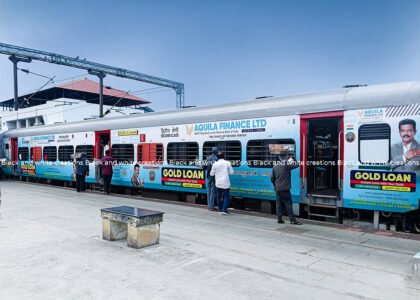Railway advertising in India featuring a passenger train with exterior branding at a railway station.